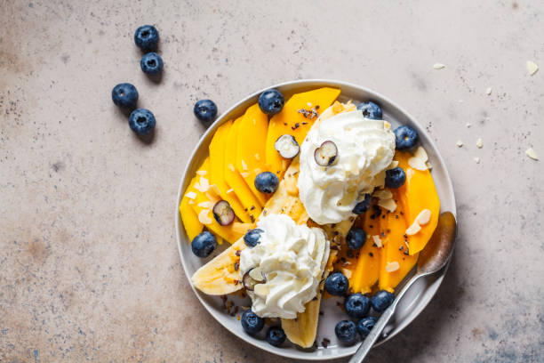 istock Healthy banana split with mango, chocolate and whipped cream on gray plate, top view. 1189960207