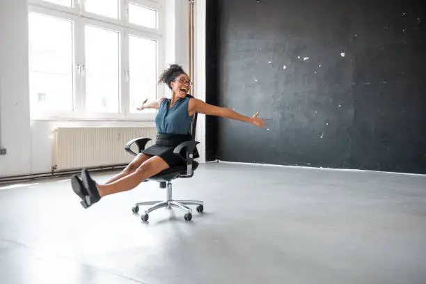 African businesswoman taking a break in the office and rolling on the office chair