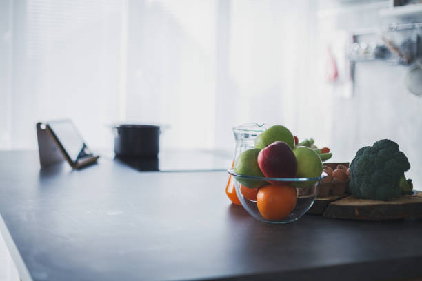 Copy space shot of abundance of fresh fruit and veg on an empty kitchen counter next to the digital tablet that is used for food preparation recipes.