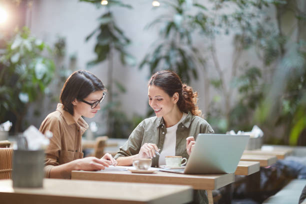 mujeres jóvenes contemporáneas trabajando en cafe - computer laptop couple women fotografías e imágenes de stock