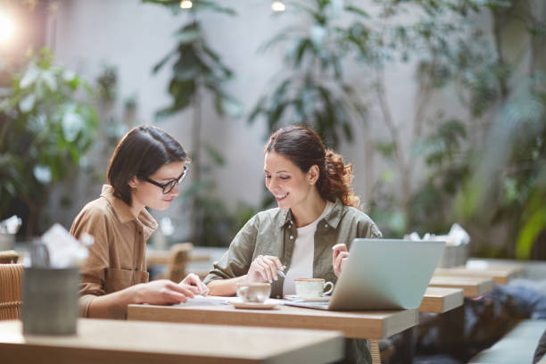 Contemporary Young Women Working in Cafe Portrait of two cheerful young omen enjoying work in beautiful outdoor cafe, copy space casual clothing stock pictures, royalty-free photos & images