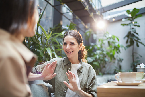 Waist up portrait of smiling young woman talking to friend on outdoor cafe terrace, copy space