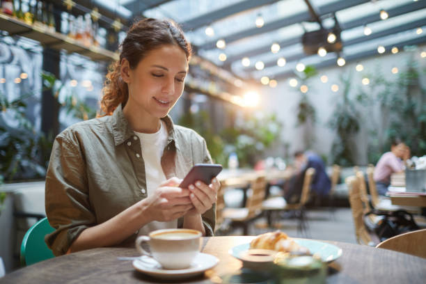 Beautiful Woman in French Cafe Portrait of beautiful young woman using smartphone while enjoying evening on outdoor terrace in cafe or coffee shop, copy space women only restaurant stock pictures, royalty-free photos & images