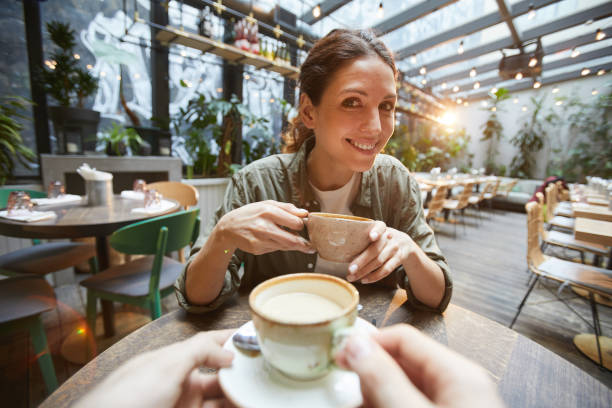 Two Women Chattering over Coffee Fisheye view of smiling woman holding coffee cup talking to friend across table in cafe, POV cappuccino photos stock pictures, royalty-free photos & images