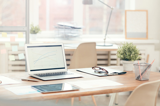 Background image of laptop on wooden table in modern office interior, workplace design concept, copy space