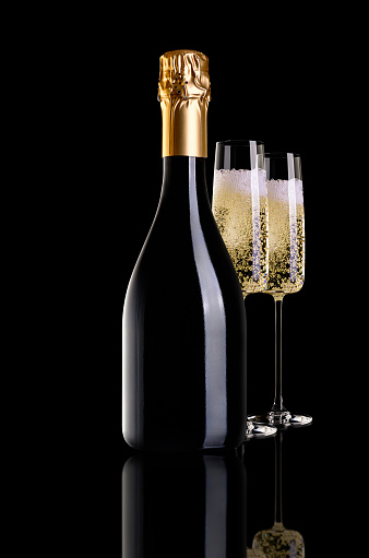A bottle of champagne and two champagne glasses isolated on a black background. Glasses are behind a bottle of champagne.