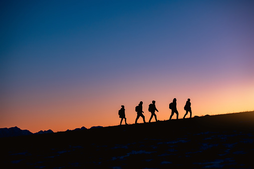 Silhouettes of group of hikers going uphill at sunset mountain
