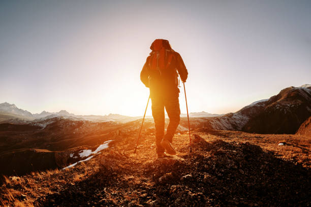 Silhouette of hiker with backpack and walking poles is going in mountains and sunset