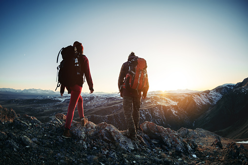Two hikers male and female walks in sunset mountains