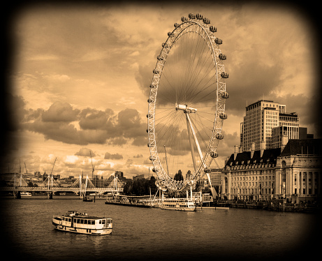 black and white, sepia toned, view from the Westminster Bridge, of the London Eye, along the Thames River, with a tour boat going by in the foreground