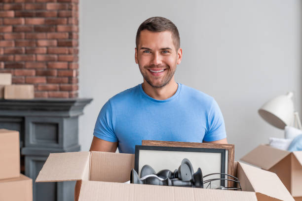 istock Cheerful young man holding cardboard boxes and smiling at camera while moving in new house 1189974926