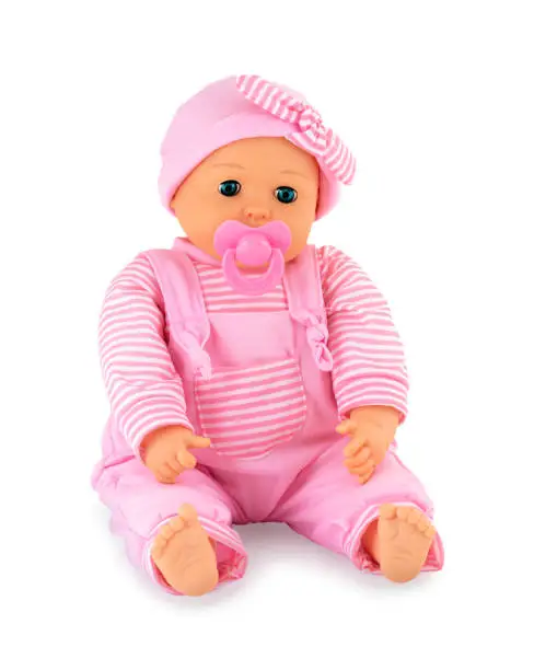 Plushie doll with blue shiny eyes isolated on white background with shadow. Sitting cute pink rag baby doll with soother on white backdrop. Baby girl plush toy with pinky cap and dummy.