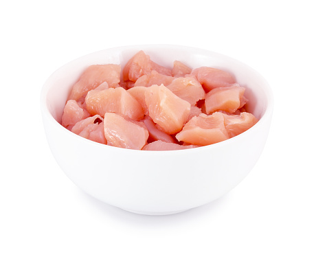 Raw chicken fillet in bowl isolated on white background with clipping path. Small pieces of raw meat on white backdrop.