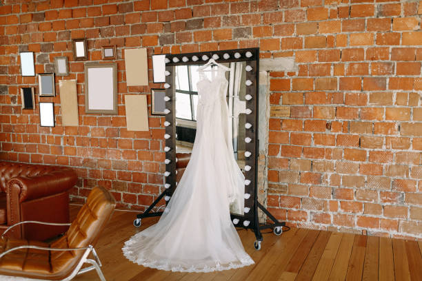 beautiful wedding dress hanging on the mirror in the great hall against the brick wall - love hanging indoors studio shot imagens e fotografias de stock