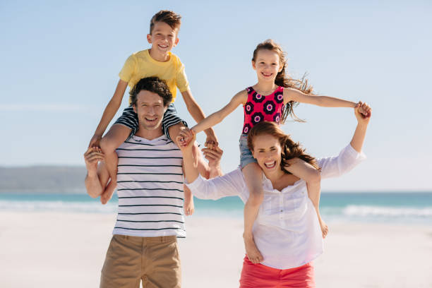 istock Smiling parents piggybacking their kids on a sandy beach 1189980624