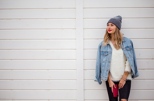 Urban style blond woman wearing hat and jeans jacket with red phone in hands, Space for text.
