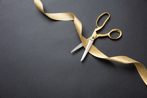 Grand opening. Gold scissors cutting gold silk ribbon, black background, top view, copy space
