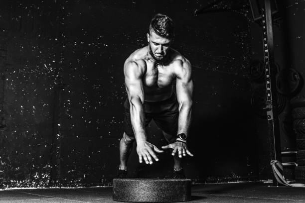 istock Young fit muscular man with big sweaty muscles doing push ups cross workout training with clap his hand above the barbell weight plate on the gym floor with motion blur black and white 1189992196
