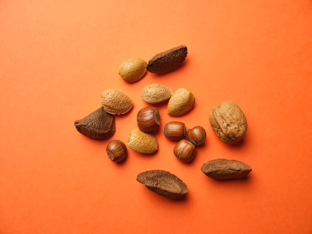 istock scattered Brazil Nuts, Hazelnuts, Walnut and Almonds against an Orange background from above. 1189994562
