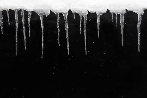 istock Winter or spring background concept. Row of icicles on wet black textured wall, with falling snow. Copy space. 1189995206