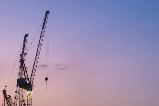 Construction cranes at sunset with copy space for ext. Purple background.