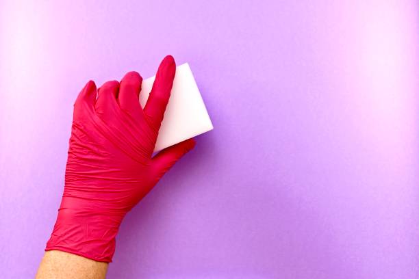 la mano izquierda en un guante de goma, un gesto de borrado, la eliminación de algo de una superficie púrpura claro, esponja de melamina. - scrub brush fotos fotografías e imágenes de stock