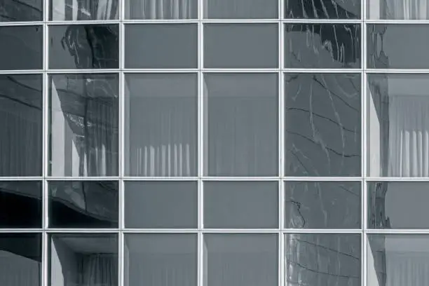 Glass wall with another building reflection. Windows are closed with curtains. Toned for black and white. May be used as business background.