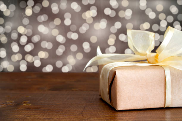 Wrapped gift with a gold ribbon on a wooden table, with a festive background.
