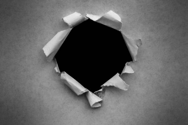 istock A hole in vintage paper with torn edges close-up with a black isolated background inside. 1190002983