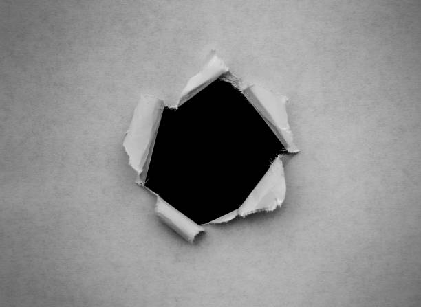 istock A hole in vintage paper with torn edges close-up with a black isolated background inside. 1190002999