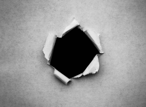 istock A hole in vintage paper with torn edges close-up with a black isolated background inside. 1190003024