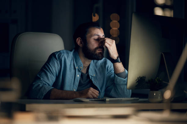 istock Tired young hipster computer programmer in casual shirt sitting at table and rubbing bridge of nose while working late in office 1190012171