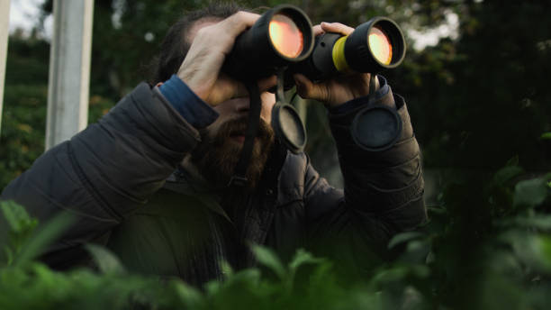 istock Young bearded man with long hair looking through binoculars in forest 1190013834