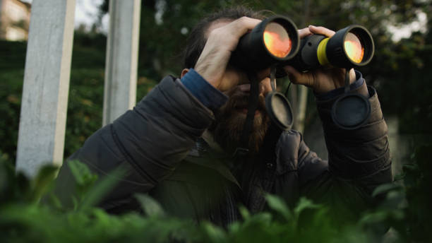 istock Young bearded man with long hair looking through binoculars in forest 1190014026
