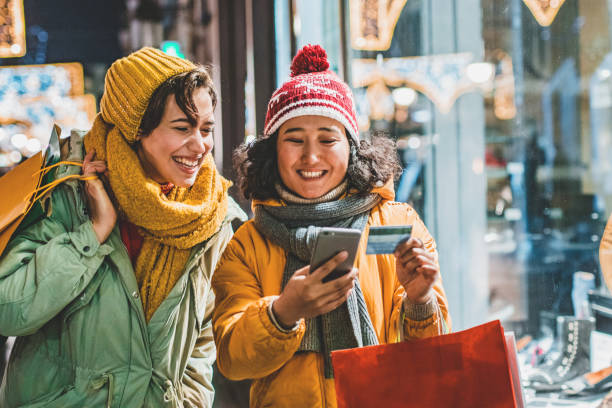 Two young woman outdoors using mobile banking for shopping