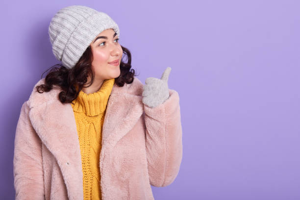 istock Image of charming magnetic young girl looking aside, making gesture, showing direction with thumb, having pleasant facial expression, wearing warm winter clothes. Copyspace for advertisement. 1190015829