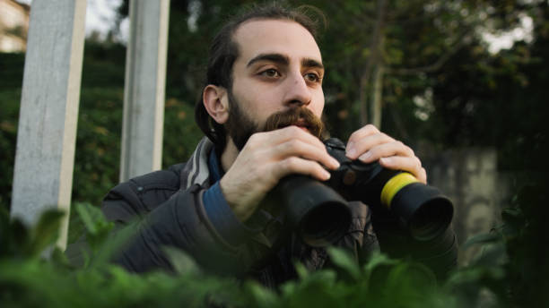 istock Young bearded man with long hair looking through binoculars in forest 1190016403