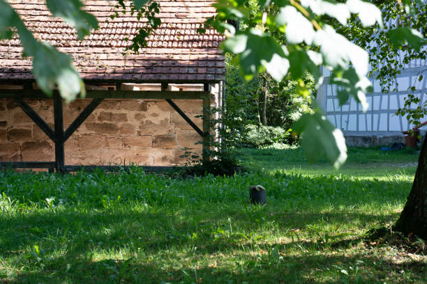 A stone shed with timber frame in an idyllic green environment, leaves in the foreground, carport