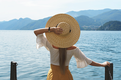 Woman is wearing straw hat looking on the beautiful Como lake
