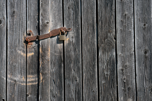 Close up of a utility shed door with a rusty padlock and weathered planks