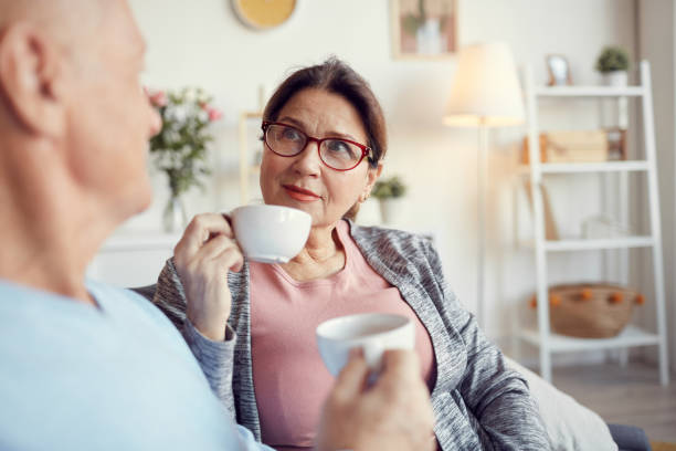 istock Content curious senior lady in glasses looking at husband while drinking tea with him at home 1190023016