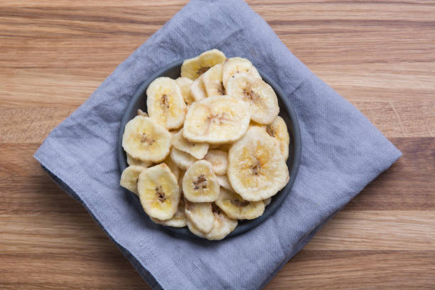 istock Dehydrated, dried banana chips on wooden board. View from above. 1190023398