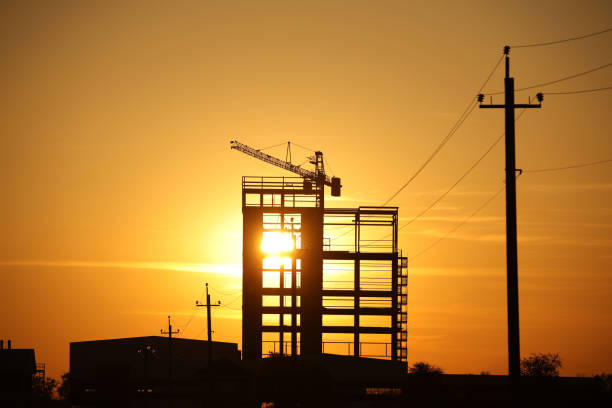 istock The skeleton of the construction of a skyscraper under construction with a tower crane against the background of an orange sky with the setting sun. Romantic landscape of a natural phenomenon.Building 1190024521