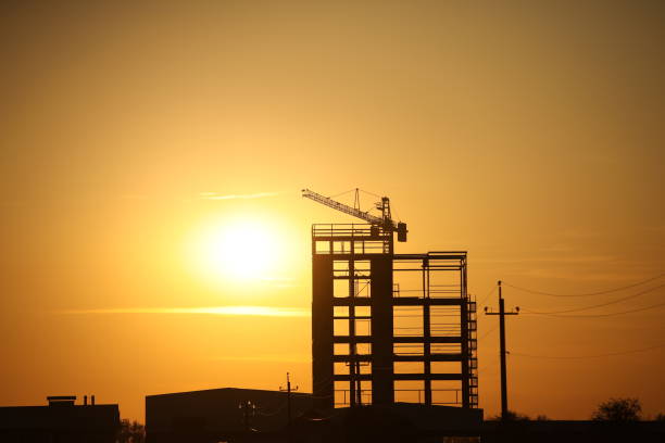 istock The skeleton of the construction of a skyscraper under construction with a tower crane against the background of an orange sky with the setting sun. Romantic landscape of a natural phenomenon.Building 1190024604