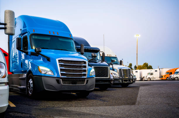 os caminhões semi dos equipamentos grandes diferentes que estão na fileira no lote de estacionamento do batente do caminhão no tempo da noite - truck parking horizontal shipping - fotografias e filmes do acervo