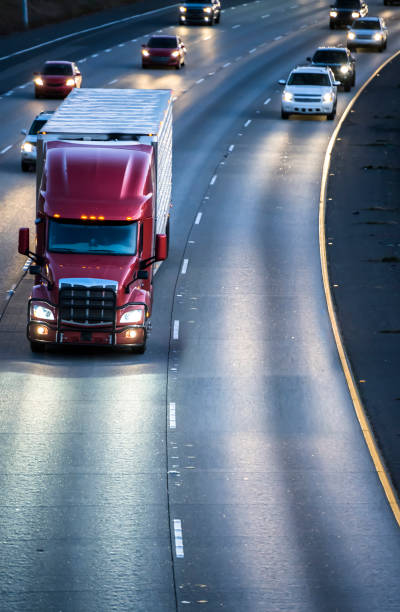 dark red big rig semi truck transporting cargo in refrigerator semitrailer running on the wide multilines highway at night with turned on headlights - highway truck road driving imagens e fotografias de stock
