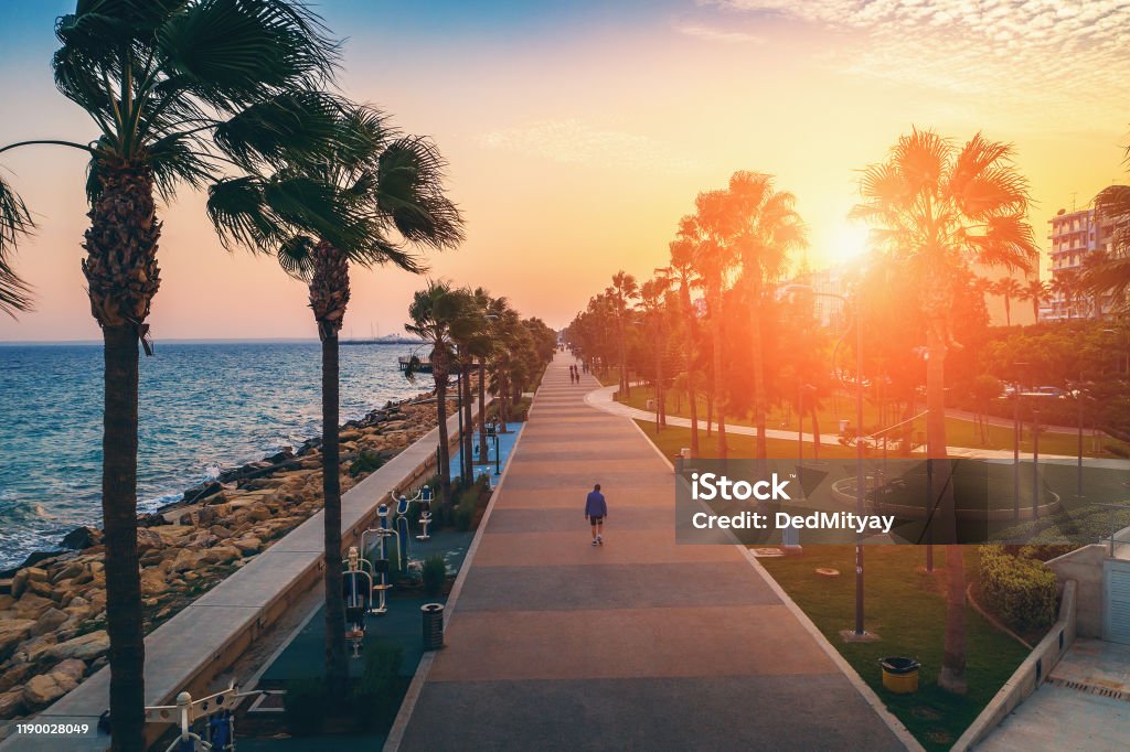 Limassol promenade or embankment at sunset. Aerial view of famous Cyprus alley with palms and walking people. Mediterranean resort in evening time Limassol promenade or embankment at sunset. Aerial view of famous Cyprus alley with palms and walking people. Mediterranean resort in evening time, toned Cyprus Island Stock Photo