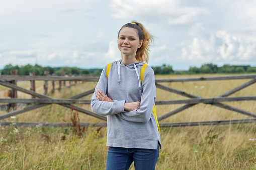 Portrait of teenage girl in gray sweatshirt with backpack with crossed arms, girl on nature, rustic style