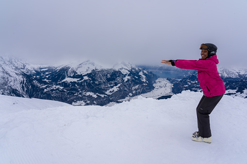 Athletic woman in ski dress and helmet makes squats on top of mountain in the snow.