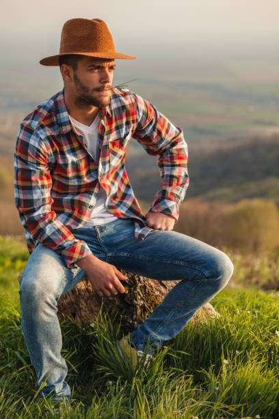 Portrait of a young man with hat and plaid shirt relaxing in nature, looking away.